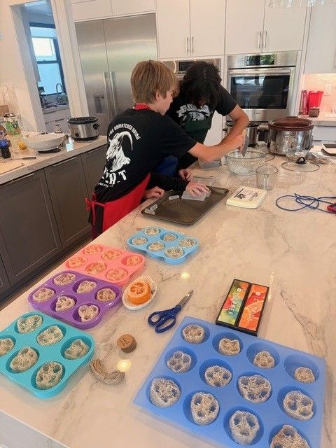 Two people pouring melted soap into molds at a kitchen counter