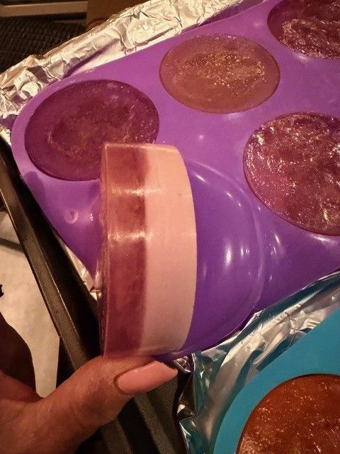 A two-layer purple and pink luffa soap bar held up in front of the mold
